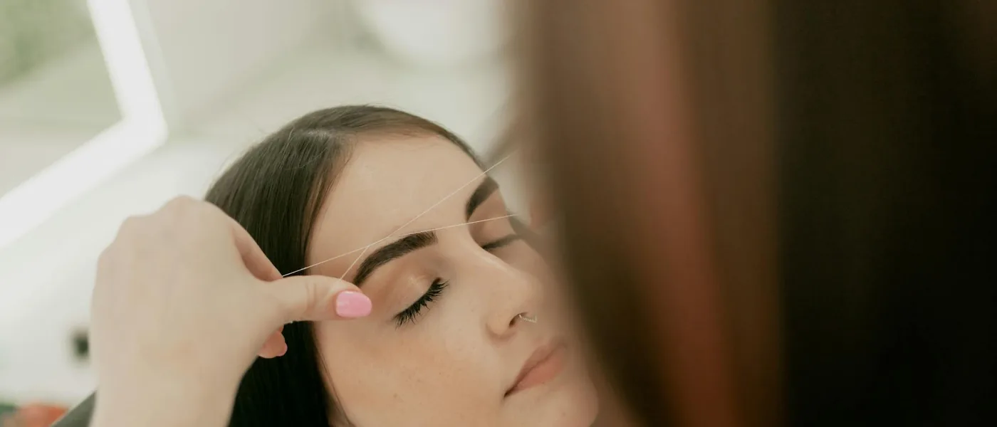 Beautician shaping a client’s eyebrows in a calm, modern salon — book threading or threading + tint at Veloura