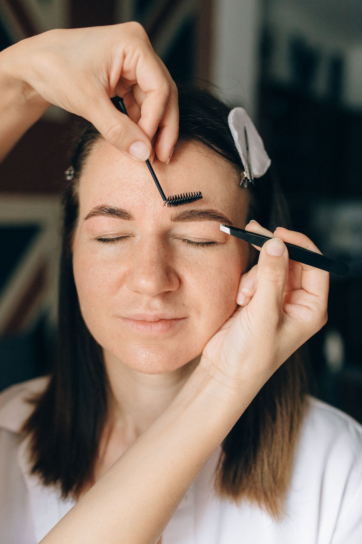 Beautician shaping a client’s eyebrows with brush and tweezers